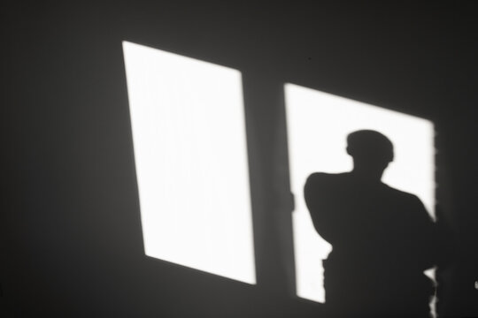 Silhouette of a man on reflected light from a window on a gray wall. Abstract background with shadow of a man. - Powered by Adobe