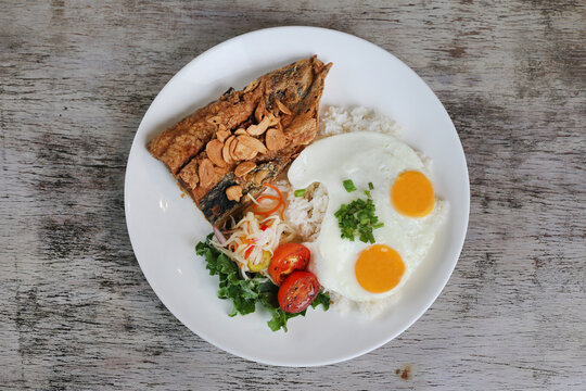 Daing Na Bangus with sunny egg and rice with tomato with salad served in dish isolated on wooden background top view of breakfast