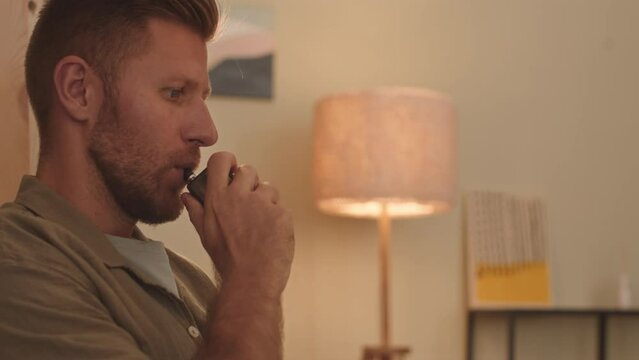 Tilt up shot of young Caucasian man vaping while working on laptop at night from home office