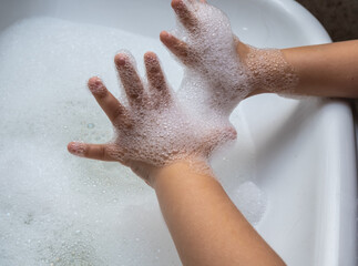 Child washing hand full of foam in bathroom sink