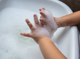 Child washing hand full of foam in bathroom sink