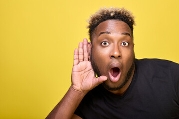 Close-up of a man eavesdropping on what others are saying. Stylish dark-skinned man in modern everyday clothes is very surprised, covers his ear with his hand, listening to rumors or gossip. 