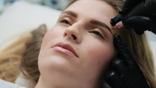 Tattoo master finishing permanent eyebrows makeup for blond model. Result of microblading