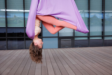 Sporty woman doing aero yoga in hammock. Brunette girl in sportswear exercising aerial yoga on...