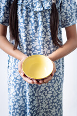A girl in a blue dress is holding an empty bowl