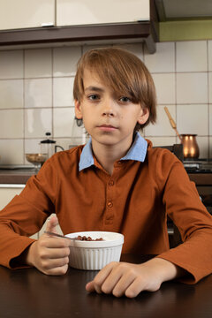 Close Up Cute Little Boy Eating Sweet Tasty Delicious Corn Cereals With Milk, Sitting At Wooden Table In Kitchen, Breakfast In Morning, Holding Spoon