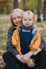 Fototapeta na wymiar Happy caucasian woman with little baby boy. Mother and son walking and having fun together among autumn leaves. Parent playing with toddler outdoors. Family, parenthood, childhood, happiness concept.