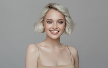 Portrait of a beautiful smiling blonde girl with a short haircut. Gray background.