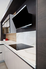 Modern gray white lacquer wood kitchen cabinet and black electric stove and hood on white granite countertop