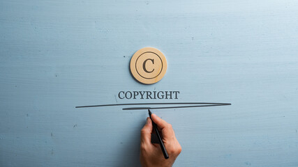 Circled letter C on a wooden cut circle with male hand writing a Copyright word under it - 537088875