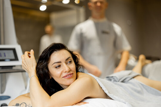 Portrait of happy adult woman lying on medical couch during vacuum roller massage procedure at medical beauty centre