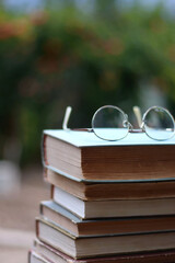 Stack of vintage hardcover books and reading glasses in a garden. Selective focus.