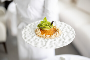 Chef holds a plate with delicious vegetarian meal decorated with flower made of avocado at restaurant of haught cuisine, close-up on dish