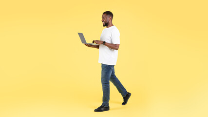 Fototapeta na wymiar African American Man Using Laptop Computer Walking Over Yellow Background