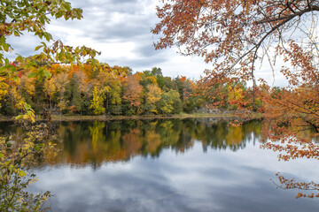 View down a calm river in autumn, fall foliage on opposite bank reflected in water, docks, cloudy, nobody	

