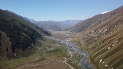 Drone shot of river between green meadows and grass hills