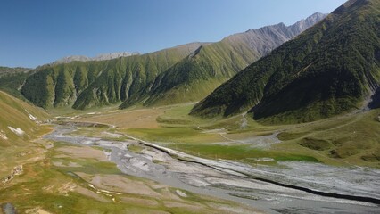 Drone shot of river between green meadows and grass hills