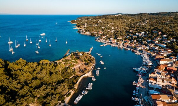 Aerial view of boats in the sea by the lush green shore with buildings on Paxos island, Greece