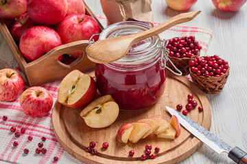 Glass jar of homemade jam from lingonberries and  red apples. Still life with fresh fruit and berries on light wooden table.