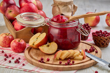 Glass jar of homemade jam from lingonberries and  red apples. Still life with fresh fruit and berries on light wooden table.