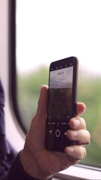  Close-up of the hands of an elderly man traveling by train and taking pictures of the landscape through the window using a smartphone, vertical video