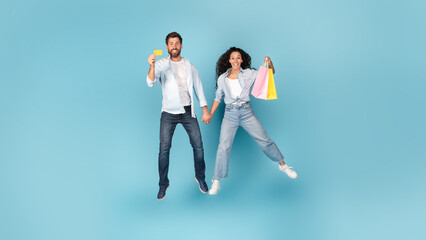 Excited glad young caucasian and arab couple with shopping bag jump in air, show credit card