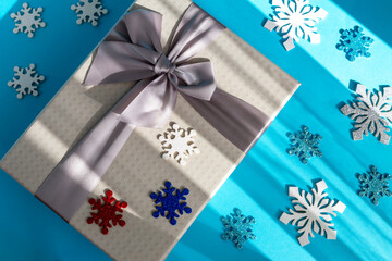 Gray gift box with bow and colorful big and small snowflakes on blue background