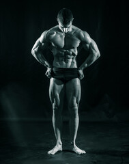 Fototapeta na wymiar Handsome bodybuilder doing classic double biceps pose, looking away, on dark background