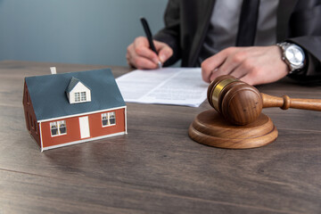 The hand of a judge with a gavel and a model of a house mediating property disputes in court