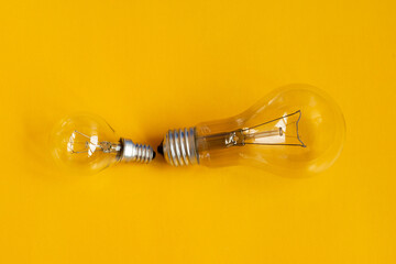 Electric light bulbs big and small on a yellow background. Conceptual idea symbol. Energy saving