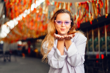 A girl in a dress, jacket and purple sunglasses poses at the festival. Woman blow kiss to camera.