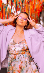 Funny photo of a beautiful fashionable girl at the festival on the background of confetti. Stylish purple raincoat and glasses.