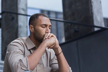 Close-up photo portrait of upset office worker fired businessman in depression, man with closed eyes sitting on stairs of office building outside.