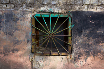 Photograph of the bars on the small square basement window. An old rusty green lattice in the form of rays of the sun diverging from the center. The concept of protection against penetration and theft