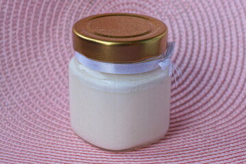 one white scented candle in a glass jar closed with a brown lid stands on a pink table