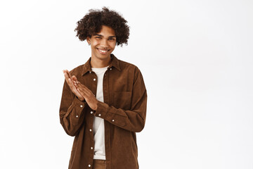 Pleased young guy smiles, applauses, praise and compliment you, clap hands, stands over white...