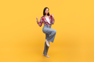 Fototapeta na wymiar Excited asian lady celebrating success and jumping in air, happy having fun over yellow studio background, full length