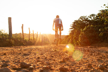 Homem andando de bicicleta em uma estrada de terra no pôr do sol