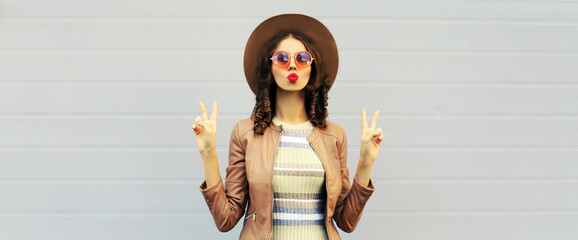 Portrait of beautiful young woman blowing her lips sending air kiss wearing knitted dress, jacket,...