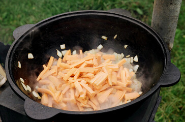 Carrots are poured into the cauldron where onions and meat are fried, mixed with a slotted spoon.
