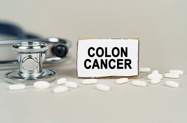 On a gray background, a stethoscope, pills and a cardboard plate with the inscription - Colon cancer