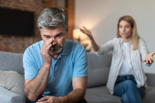 Angry middle aged european woman scolding at offended man during quarrel in living room interior
