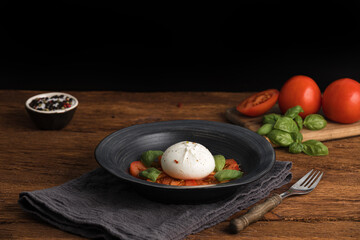 Fresh Italian burrata with tomatoes and basil on plate on wooden table, close up. Burrata cheese ball made from mozzarella and cream. Healthy food