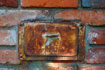 An image of a rustic brick wall with rusted metal box insert. 