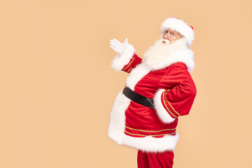 Fototapeta na wymiar Santa Claus posing on beige studio background, showing on an empty space for your text. Xmas sale, discount concept. Christmas time. Have you been a good girl/boy this year?