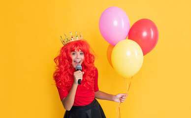 glad child in crown with microphone and party balloon on yellow background