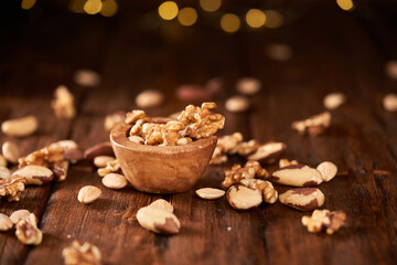 Mixed nuts on a brown wooden table and yellow bulbs on a blurry background.