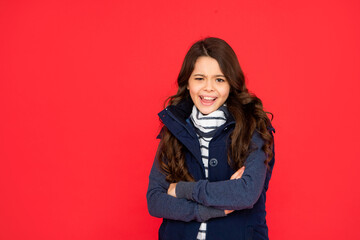 emotional kid with curly hair in puffer waistcoat. teen girl on red background. portrait of child