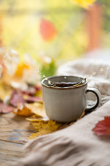 Cozy autumn concept. A cup of tea with flying splashes on the windowsill against the background of glass with raindrops