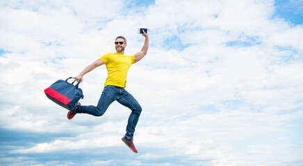 Fototapeta na wymiar Active man jumping with travel bag midair sky background, copy space